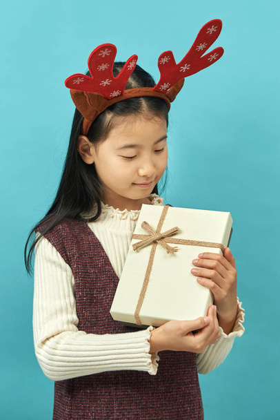 Aziatisch meisje met een kerst concept hoofdtooi kind, Close up van schattig klein Aziatisch meisje op blauwe achtergrond, geïsoleerd. - Foto, afbeelding