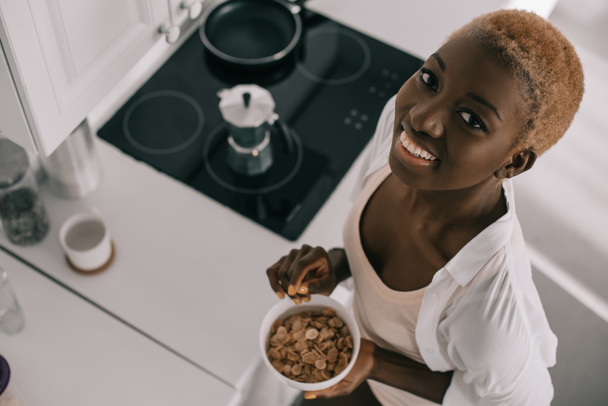 felülnézete vidám afrikai-amerikai nő, mosolygós és a gazdaság tál kukoricapehely  - Fotó, kép