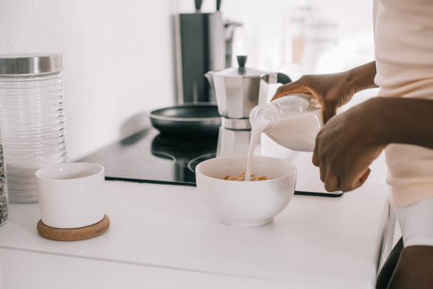vista ritagliata di donna afro-americana versando latte in ciotola con cornflakes in cucina
  - Foto, immagini