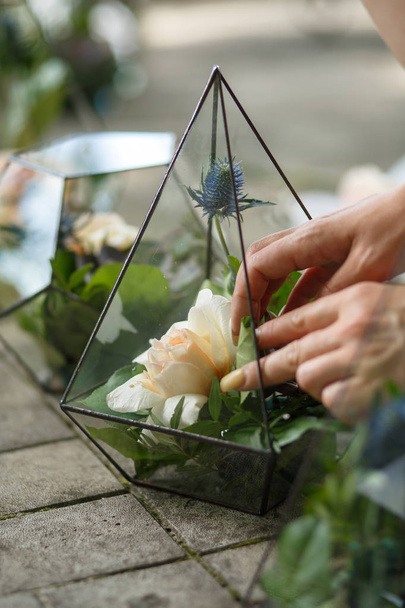 θηλυκό ανθοπωλείο βάζει φρέσκα χυμώδη και τριαντάφυλλο λουλούδια σε γυάλινο ανθοπωλείο. Εκδήλωση φρέσκα λουλούδια διακόσμηση. Ανθοπωλείο ροή εργασίας. Σχεδιασμός δεξιώσεων γάμου - Φωτογραφία, εικόνα