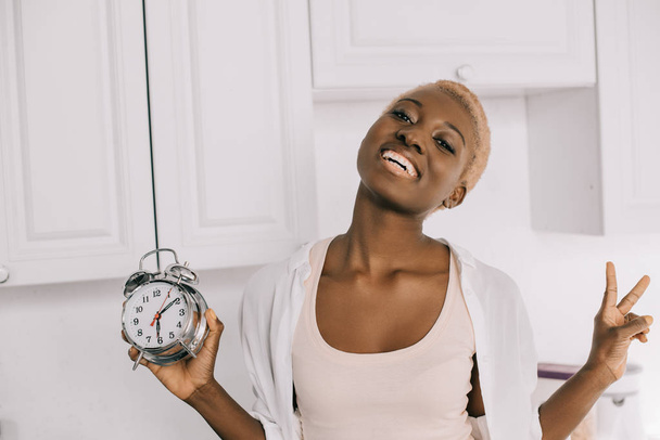 iloinen afrikkalainen amerikkalainen nainen tilalla kello ja osoittaa rauhan merkki
 - Valokuva, kuva