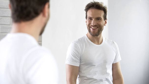 Cheerful man looking at reflection in mirror, motivating for success during day - Φωτογραφία, εικόνα