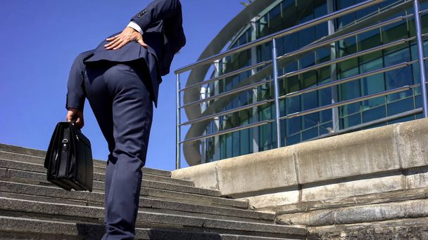 Manager in suit suffering from lower back pain, slipped disc, disease symptom - 写真・画像