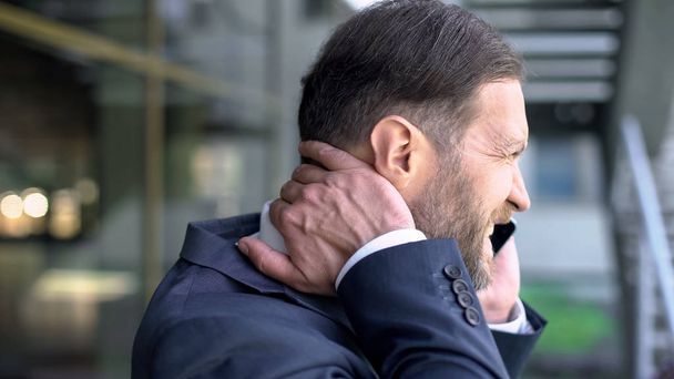 Middle-aged man suffering neck pain, talking on phone, spinal problem, body - Foto, Bild