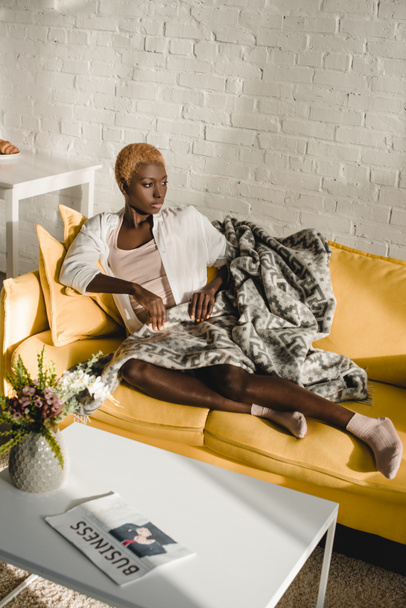 mujer afroamericana confiada acostada en un sofá amarillo en la sala de estar
  - Foto, imagen