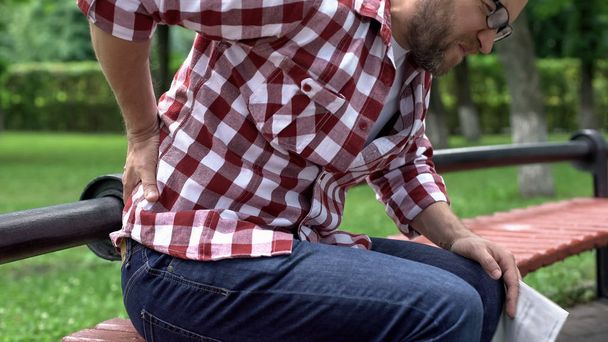 Man feeling lower back pain, reading newspaper in park, compressed nerve roots - Foto, imagen