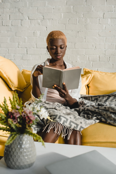 attractive african american woman reading book on yellow sofa  - Photo, Image