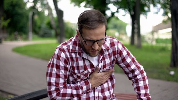 Male suffering sudden chest pain, sitting on bench in park, cardiology, health - Φωτογραφία, εικόνα
