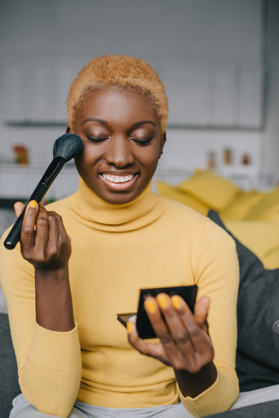smiling african american woman applying powder with cosmetic brush  - 写真・画像
