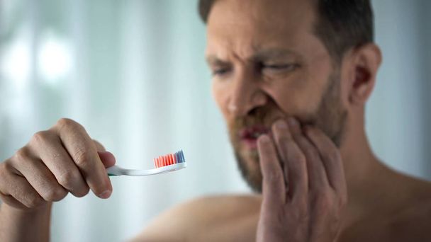 Male in bathroom looking at blood toothbrush, oral hygiene, parodontosis illness - Φωτογραφία, εικόνα