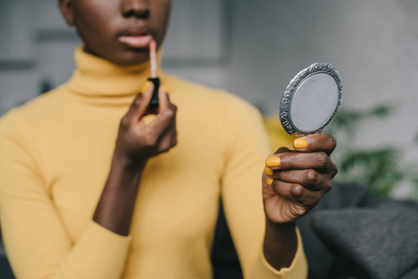 selective focus of african american woman holding mirror and applying lip gloss - 写真・画像