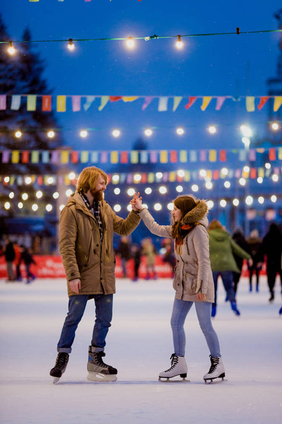 Uzun saçlı sarışın saçlı beyaz adam genç çift tr ve eğlenceli, aktif tarihi buz pateni Buz arenada akşam şehir meydanında Noel arifesinde kışın sakal ve güzel bir kadın var - Fotoğraf, Görsel