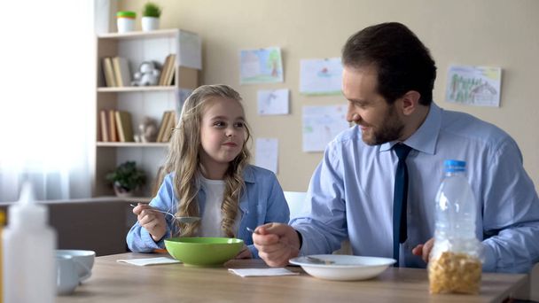 Friendly daughter and dad eating cereal with milk, breakfast, healthy nutrition - Foto, Imagen
