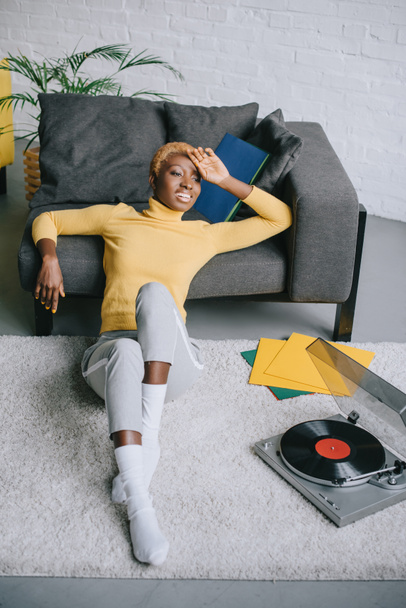 african american woman with short hair sitting on carpet near record player - Foto, Bild