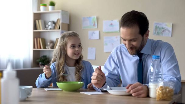 Caring father and little daughter eating cornflakes and talking, morning ritual - Foto, Imagen