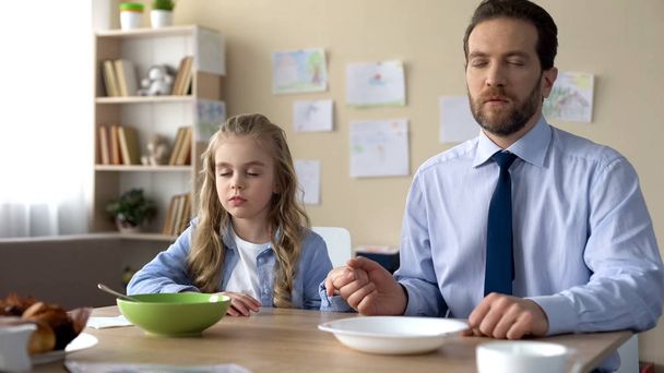 Pretty girl and her father praying before eating breakfast, spiritual education - Фото, изображение