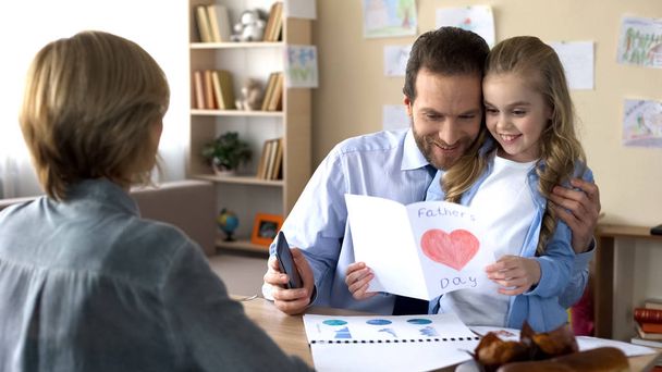 Busy father stopping phone conversation to look at daughters greeting card - Фото, зображення