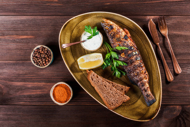 レモンと木製の背景に皿の上の緑と焼き魚。魚介類のおいしい料理。トップ ビュー - 写真・画像