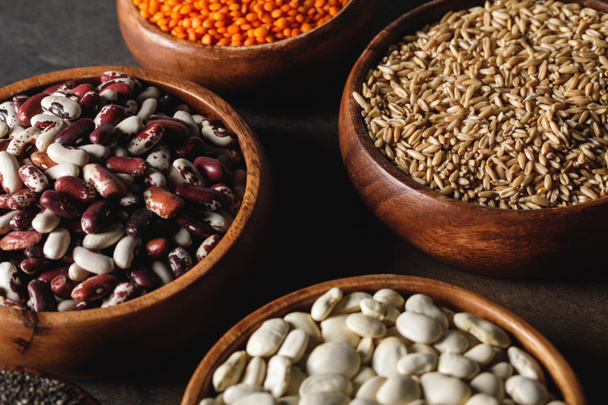 variety of beans in wooden bowls with oat groats on table  - Photo, Image