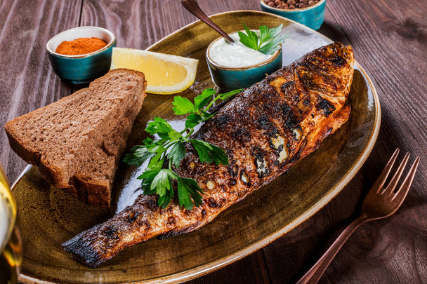 Baked fish with lemon and greens on plate on wooden background. Delicious dish of seafood - Foto, afbeelding
