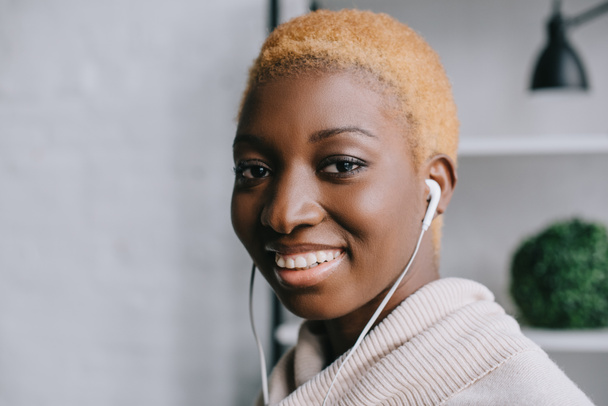 close up of smiling african american woman listening music in earphones - Фото, изображение