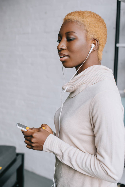 selective focus of dreamy african american woman listening music in earphones - Photo, image