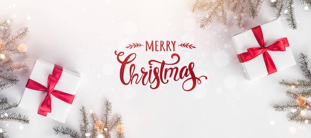 Счастливого Рождества Типографика на белом фоне с подарочными коробками, еловыми ветвями, красным декором. Рождество и новогодняя открытка, боке, свет. Плоская кладка, вид сверху, широкий состав
 - Фото, изображение