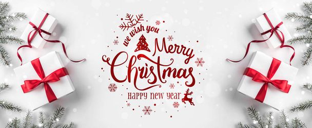 Feliz Navidad tipográfica sobre fondo blanco con cajas de regalo, ramas de abeto, decoración roja. Tarjeta de Navidad y Año Nuevo, bokeh, luz. Piso tendido, vista superior
 - Foto, Imagen