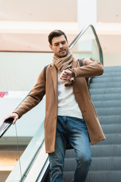 hombre guapo en bajar en escaleras mecánicas y mirando el reloj en el centro comercial
 - Foto, imagen