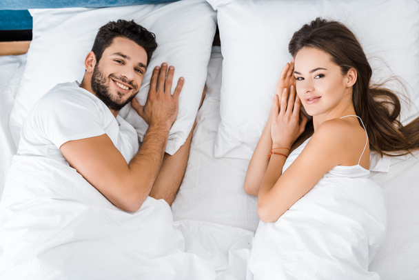 Draufsicht auf ein junges Paar, das im Bett liegt und in die Kamera schaut - Foto, Bild