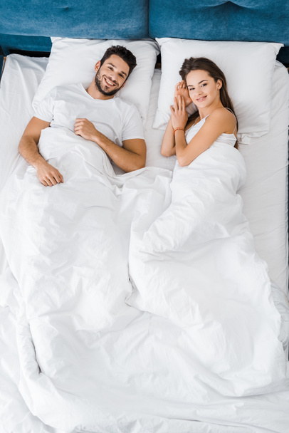 top view of cheerful smiling couple lying in bed together - Foto, immagini