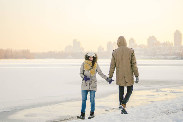 テーマ クリスマス休日冬正月。カップルを愛する若いスタイリッシュな白人 Heteresexual 凍った湖の海岸の上を歩きます。日付。夕暮れ時の冬のバレンタインの日。愛とロマンスのテーマ. - 写真・画像