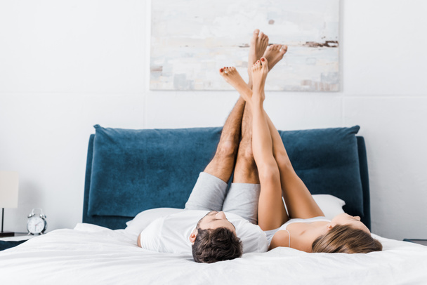 young boyfriend and girlfriend lying with raised legs in morning - Фото, зображення