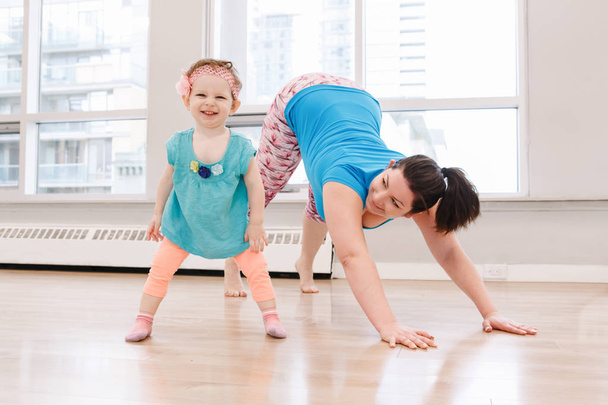 Young woman with child daughter doing workout in gym class to loose baby weight. Child-friendly fitness for mothers with kids toddlers. Lifestyle concept of family activity indoors. - Photo, Image