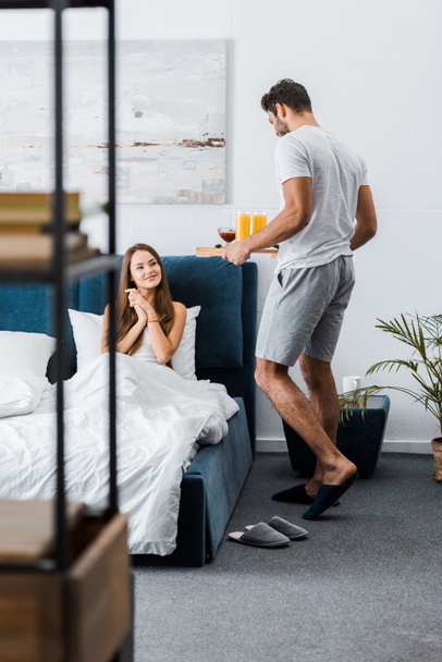 young man giving tray with breakfast to girlfriend in bed - Foto, afbeelding