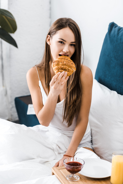 attractive girl eating sweet croissant in bed - Foto, afbeelding