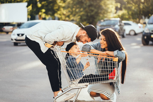 Young parents put their son in a cart and have fun in the parking. - Fotografie, Obrázek
