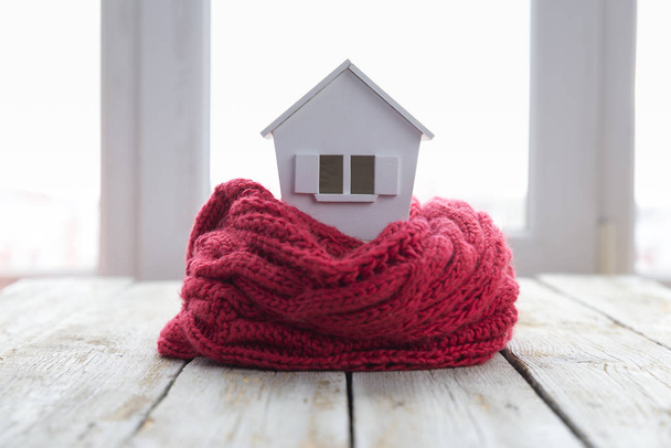 house in winter - heating system concept and cold snowy weather with model of a house wearing a knitted cap - Фото, зображення