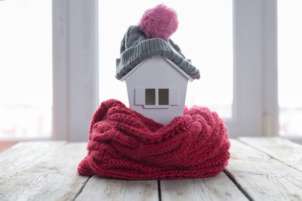το σπίτι το χειμώνα - θέρμανσης σύστημα έννοια και κρύο χιονισμένο καιρικές συνθήκες με το μοντέλο του ένα σπίτι φορώντας ένα πλεκτό κάλυμμα - Φωτογραφία, εικόνα