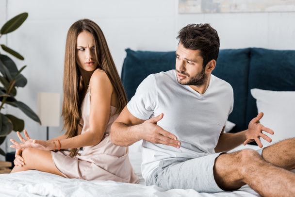 unglückliches frustriertes Paar im Schlafanzug, das Rücken an Rücken auf dem Bett sitzt und wütend gestikuliert, Konzept sexueller Probleme - Foto, Bild