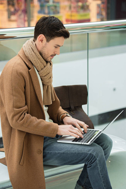 handsome man sitting on bench and typing on laptop keyboard - Foto, afbeelding