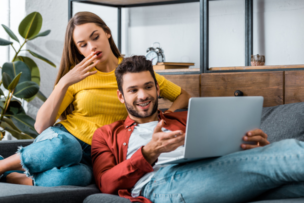 young surprised couple sitting on sofa and using laptop - Φωτογραφία, εικόνα