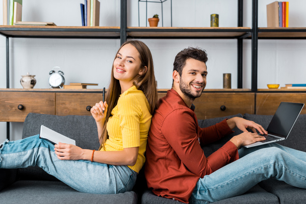 young happy couple sitting in livingroom with notebook and laptop and smiling at camera - Φωτογραφία, εικόνα