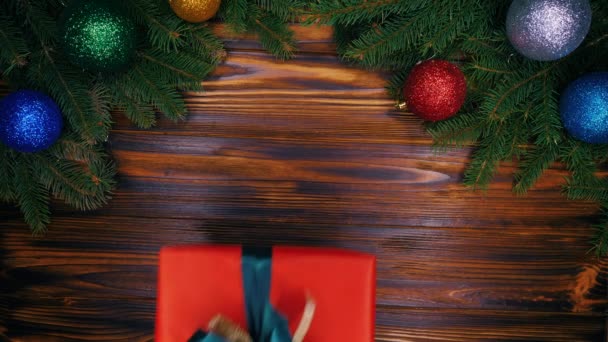 Closeup şerit ahşap arka plan üzerinde kırmızı Noel Hediyelik kutu tutan kadın. Üstten görünüm, düz yatıyordu. Tatil, kutlama, hediyeler, mutluluk kavramı. Baubles, çam dalları. - Video, Çekim