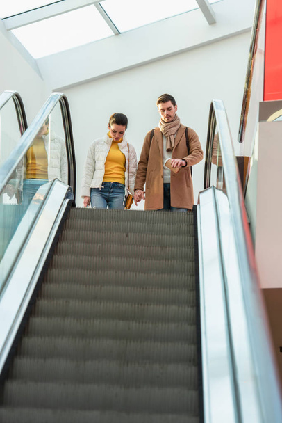 attractive girl and handsome man standing at top of escalator - Zdjęcie, obraz