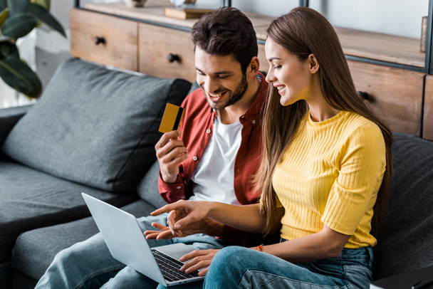 happy man holding credit card and doing online shopping near girlfriend - Photo, Image