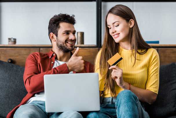 happy woman holding credit card while boyfriend showing thumb up sign - Φωτογραφία, εικόνα