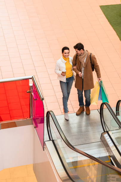 casal amoroso com sacos de compras perto escada rolante no shopping
 - Foto, Imagem