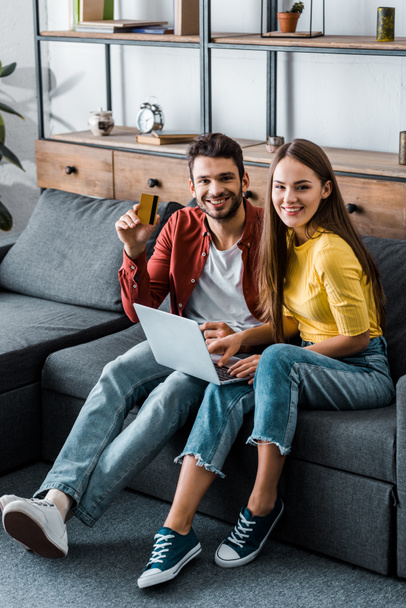 cheerful boyfriend and girlfriend doing online shopping on sofa in living room - Фото, изображение