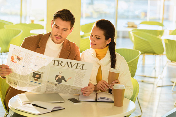 handsome man and smiling girl reading travel newspaper in cafe - Photo, Image